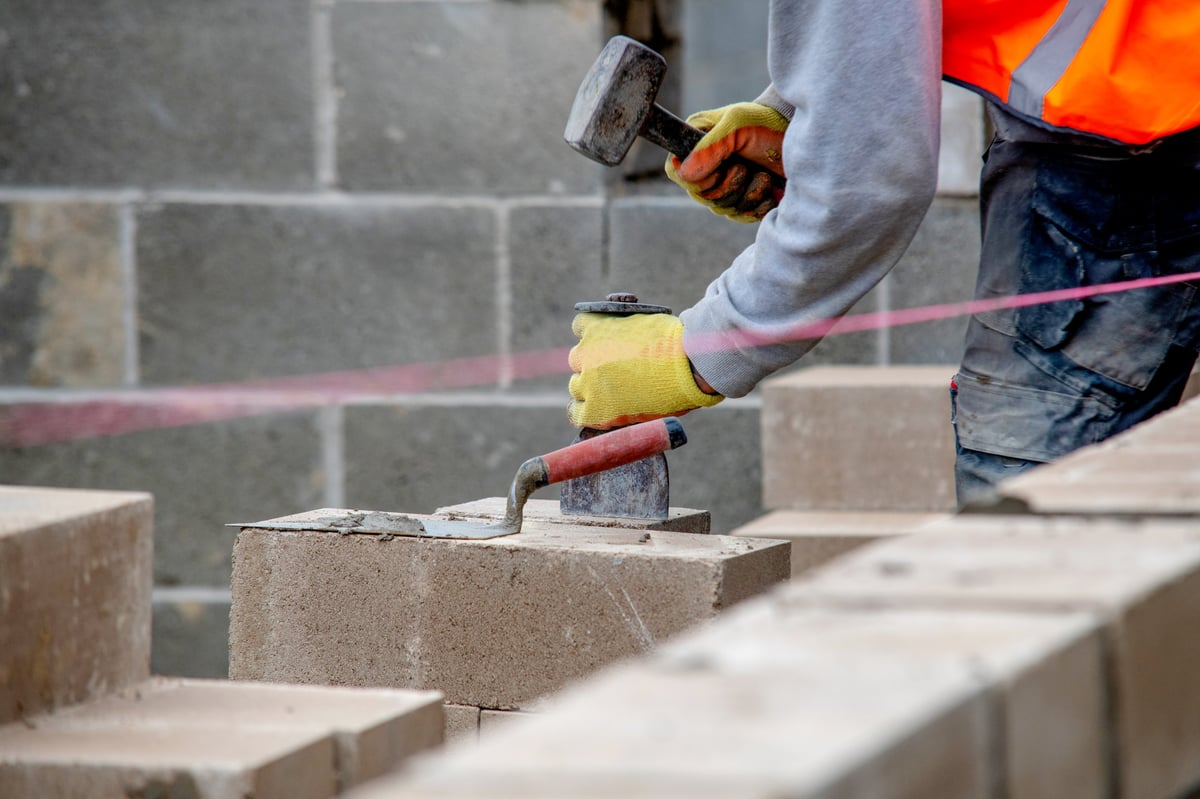 Bricklayer placing bricks with a hammer and trowel on a building site